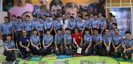 Colégio da Polícia Militar do Paraná visita TRE-PR Fotografia de um grupo de alunos vestindo uniforme azul. Atrás deles há um banner com a foto de ...