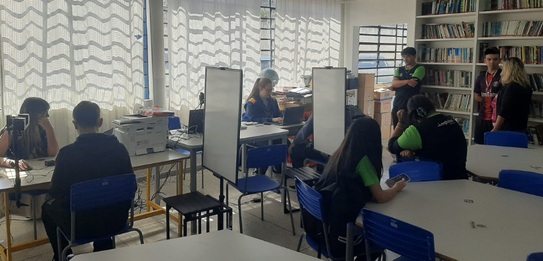Fotografia de uma mulher em pé palestrando para jovens uniformizados em uma sala de aula com par...