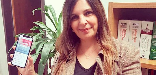 Com foco na integração e na sustentabilidade, grupo Desapego TRE-PR reúne servidores Foto de uma servidora segurando um celular. Atrás dela, há uma estante com livros de Direito