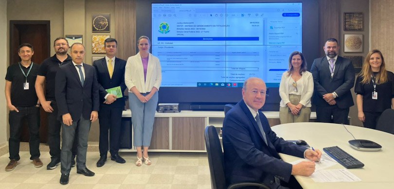 Fotografia de uma sala de trabalho. Há um homem de terno e gravata sentado em uma mesa de reuniõ...