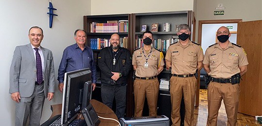 Fotografia de um grupo de policiais militares e civis, lado a lado. Eles estão em um escritório....