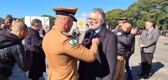 Na foto, policiais militares dirigem um carro oficial, sobre o qual homens em trajes especiais c...
