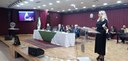 Fotografia do auditório do TRE-PR. No palco, é possível ver a mesa de autoridades e uma mulher f...