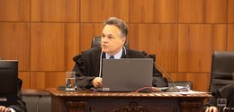 Fotografia do desembargador Luiz Osório Moraes Panza diante de uma mesa de madeira sobre a qual ...