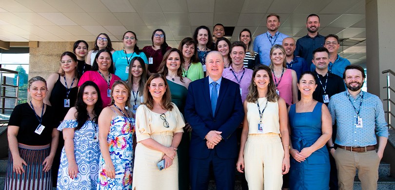 Homens e mulheres posam sorridentes para a foto. Eles estão em uma escada, de forma que estão di...