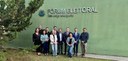 Fotografia de quatro mulheres e sete homens posando sorrindo em frente ao Fórum Eleitoral Des. J...