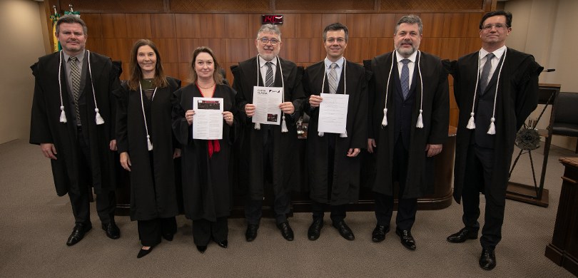 Corte do TRE-PR assina Carta Supera para promover a inclusão política Cinco homens e duas mulheres posando para a foto. Eles usam togas e as pessoas no meio estão seg...