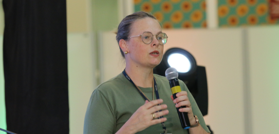 Fotografia de nove pessoas, entre homens e mulheres, posando sorrindo em frente a um edifício co...