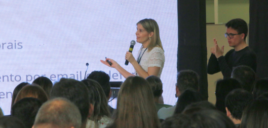 Fotografia de nove pessoas, entre homens e mulheres, posando sorrindo em frente a um edifício co...