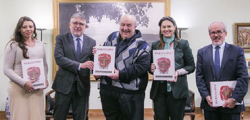 Fotografia de duas mulheres e três homens posando em uma sala com paredes brancas e diversos qua...