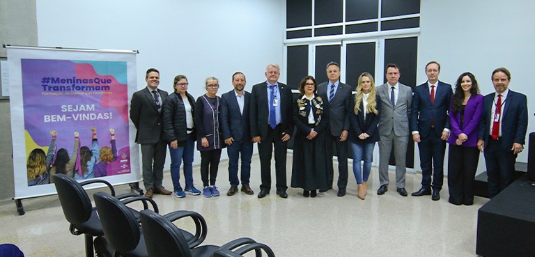 Fotografia em que se veem autoridades, professoras e servidores posando em uma sala com paredes ...