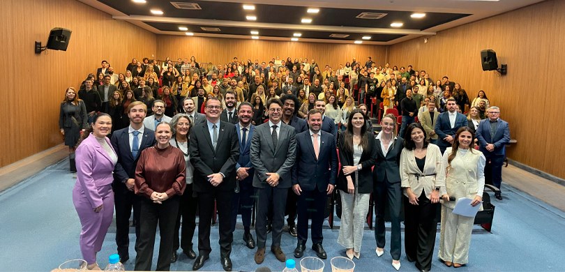 Fotografia em que se observa um grande grupo de pessoas reunidas em um auditório para um registr...