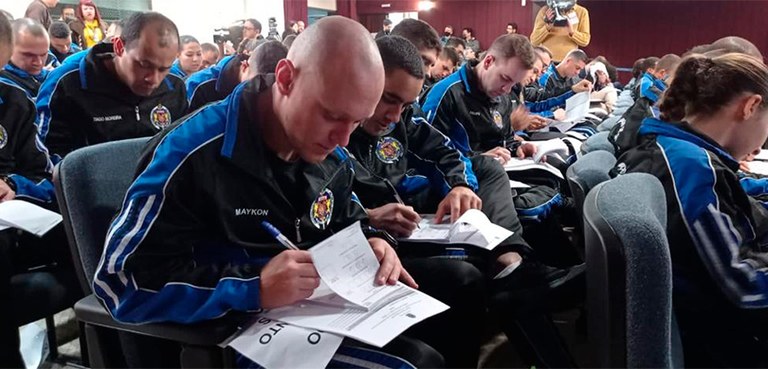 Fotografia dos cadetes na platéia do auditório do TRE-PR. Eles estão preenchendo algumas folhas.