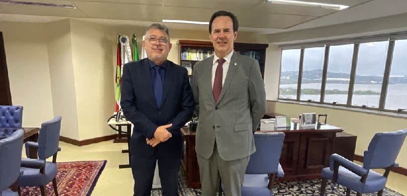 Des. Coimbra de Moura se encontra com presidente do TRF4 1 Fotografia de dois homens de terno posando sorrindo em uma sala com paredes brancas. Ao fundo, m...