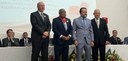 Fotografia de quatro homens de terno posando sorrindo. Um deles usa uma medalha no pescoço. Ao f...