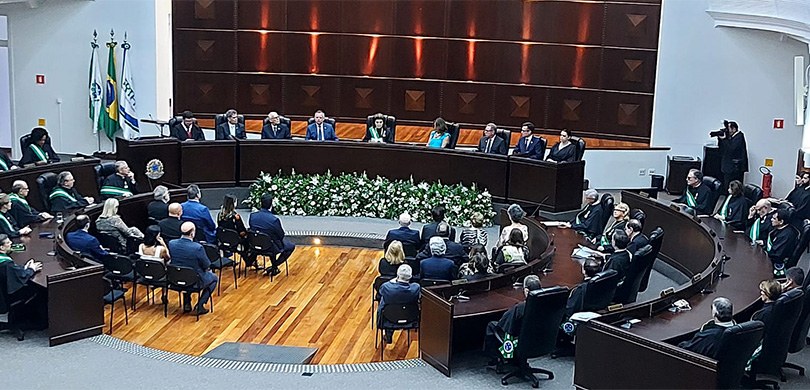 Fotografia do plenário do TRT-PR, com as mesas de autoridades organizadas em formato circular. A...