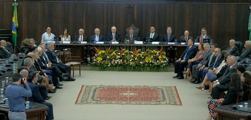 Fotografia da mesa de autoridades no plenário do TJPR. Na frente da mesa, há um arranjo de flore...