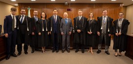 Fotografia de três mulheres e sete homens posando sorrindo na sala de sessões do TRE-PR. Todos v...