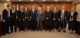 Fotografia de três mulheres e sete homens posando sorrindo na sala de sessões do TRE-PR. Todos v...