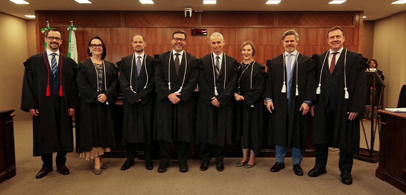 Fotografia em que se observa um homem de pele clara, cabelos e barba curtos e escuros, usando óc...