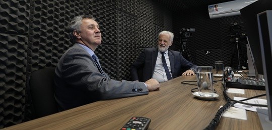 Desembargador Gebran defende a segurança do voto e comenta competência da Justiça Eleitoral para julgamento de crimes de Caixa 2 Fotografia de duas pessoas sentadas atrás de uma mesa em um estúdio de rádio