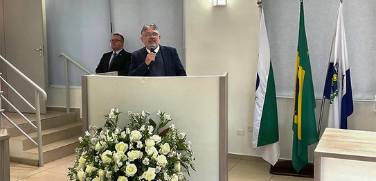Fotografia de quatro homens sentados atrás de uma mesa de autoridades. Todos usam terno. Ao redo...