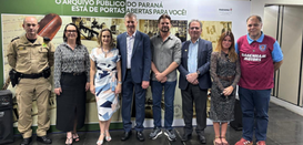 Três mulheres e cinco homens perfilados posam para a foto. Ao fundo vê-se um painel onde se lê: ...