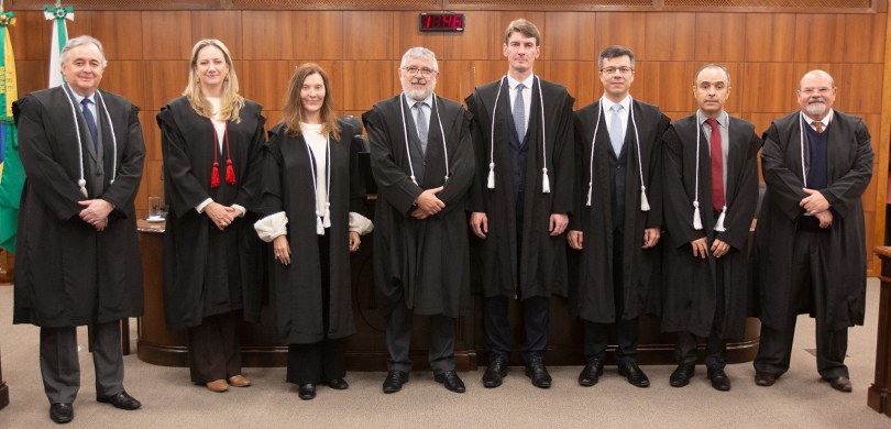Fotografia dos membros da Corte do TRE-PR posando para foto na sala de sessões. Ao fundo, as ban...