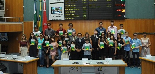 Fotografia de um grupo de estudantes e vereadores segurando a constituição brasileira. Eles estã...