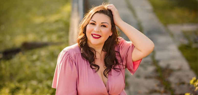 Fotografia de uma mulher posando sorrindo para foto. Ela está com a mão esquerda na cabeça. A mu...