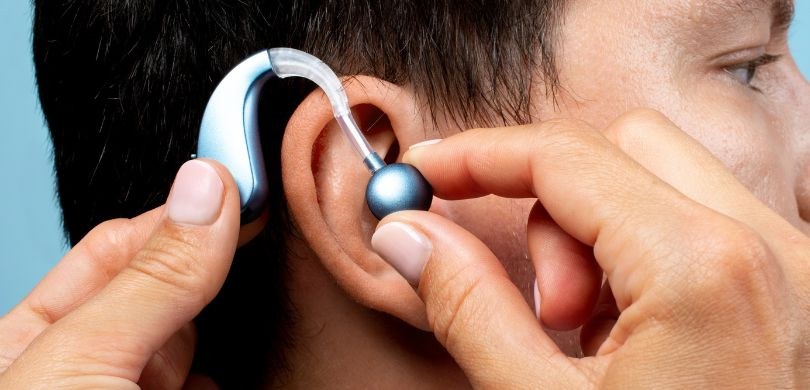 Dia Nacional de Prevenção e Combate à Surdez é celebrado nesta segunda-feira (10) fotografia em que se vê o perfil de um homem em cuja orelha duas mãos estão colocando um aparelh...