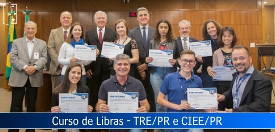 Em uma sala de sessões, foto de um grupo de pessoas segurando diplomas