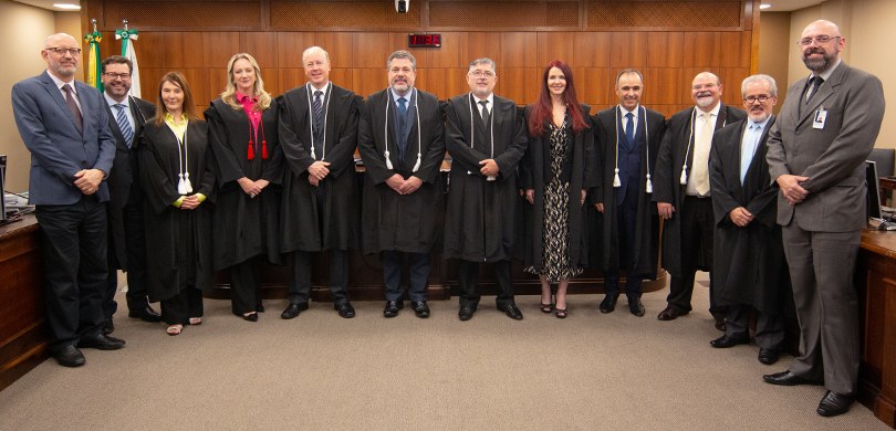 A imagem mostra a sala de sessões da Corte. Estão de pé posando para a foto nove homens e três m...