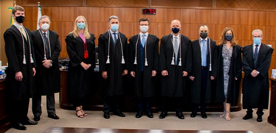 Fotografia de um grupo de magistradas e magistrados na Corte Eleitoral. Eles usam toga e olham e...