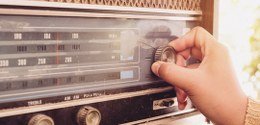 Foto de um rádio antigo e uma mão mexendo nele
