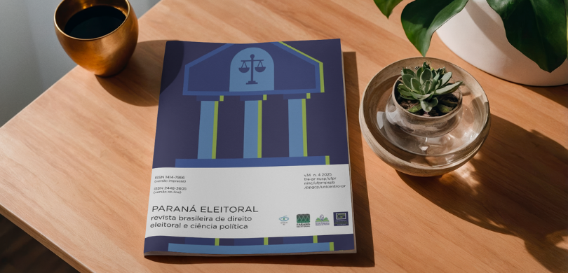 EJE-PR e UFPR lançam edição especial da Revista Paraná Eleitoral com pesquisas sobre democracia, eleições e cidadania Fotografia da edição especial da Revista Paraná Eleitoral sobre uma mesa de madeira, sobre a qua...