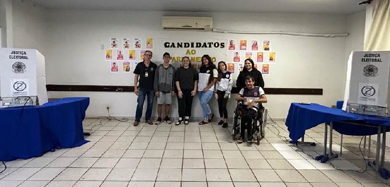 Fotografia de um homem adulto ao lado de seis estudantes (dois rapazes e quatro moças). Um dos j...