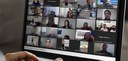 Fotografia de um notebook durante uma reunião por videoconferência. Há diversas pessoas, entre h...