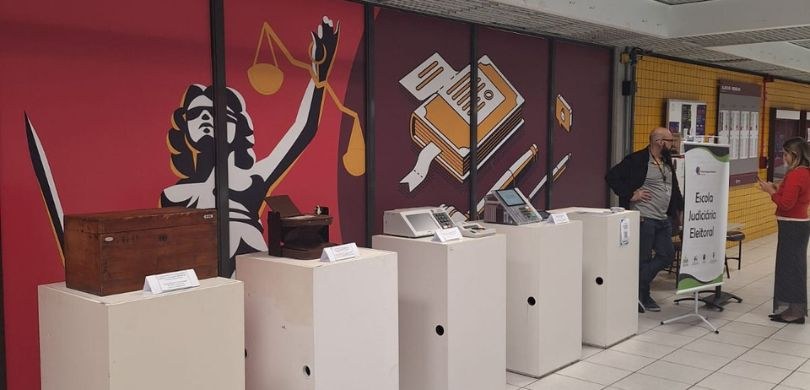 Fotografia na qual se observa um espaço de exposição institucional com objetos históricos e mode...