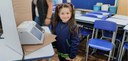 Fotografia de uma menina vestida com um uniforme escolar azul e verde sorrindo para foto em fren...