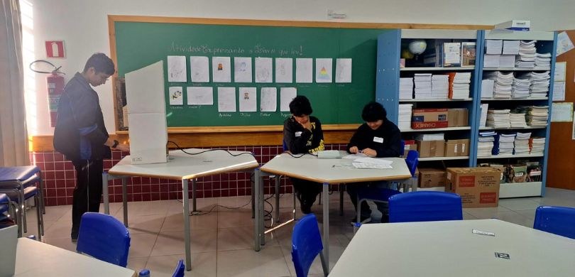 Fotografia que retrata uma simulação de votação em uma sala de aula. Em primeiro plano, observam...