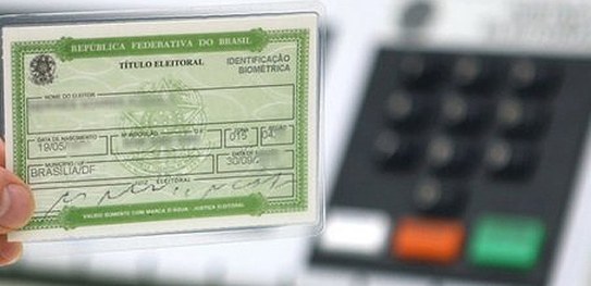 Eleitor com título cancelado deve regularizar a situação para votar em 2022 Foto de uma urna eletrônica à direita e um título eleitoral à esquerda