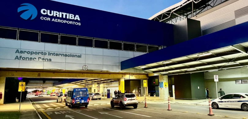 Fotografia que retrata a fachada do Aeroporto Internacional Afonso Pena. A estrutura do edifício...