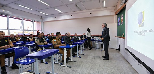 Fotografia de cinco homens sentados em uma mesa, todos eles estão vestindo terno.