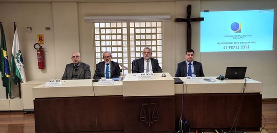 Um homem, que veste terno, está falando em um púlpito enquanto uma plateia o assiste.