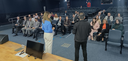 Fotografia em auditório na qual se observam diversas pessoas, homens e mulheres, distribuídas em...