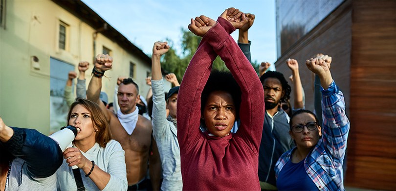 Fotografia colorida que retrata um grupo diversificado de pessoas em uma manifestação em ambient...