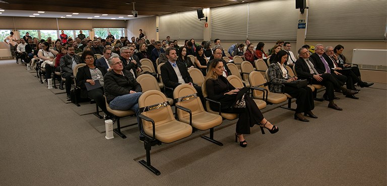 Fotografia da plateia, formada por homens e mulheres, na sala de sessões do TRE-PR. As pessoas e...