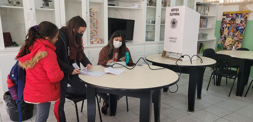 Fotografia de uma sala de aula, em que estudantes se preparam para votar na urna eletrônica.
