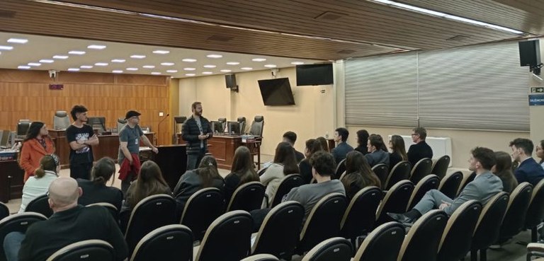 Estudantes da CESUL realizam visita acadêmica ao TRE-PR A fotografia mostra alunas e alunos sentados nas poltronas de um auditório. À frente, três homen...